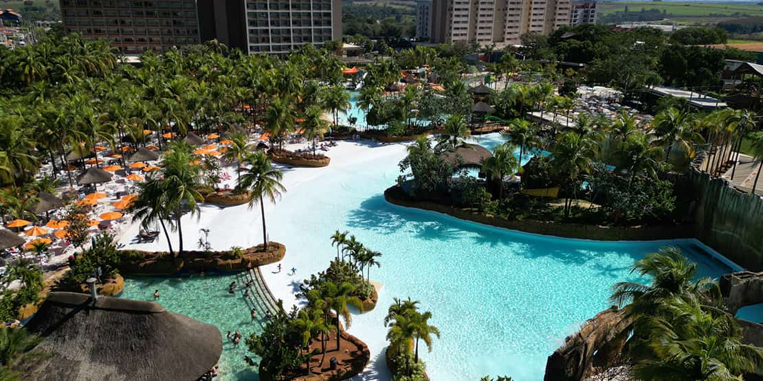 piscina em meio a coqueiros com resorts ao fundo
