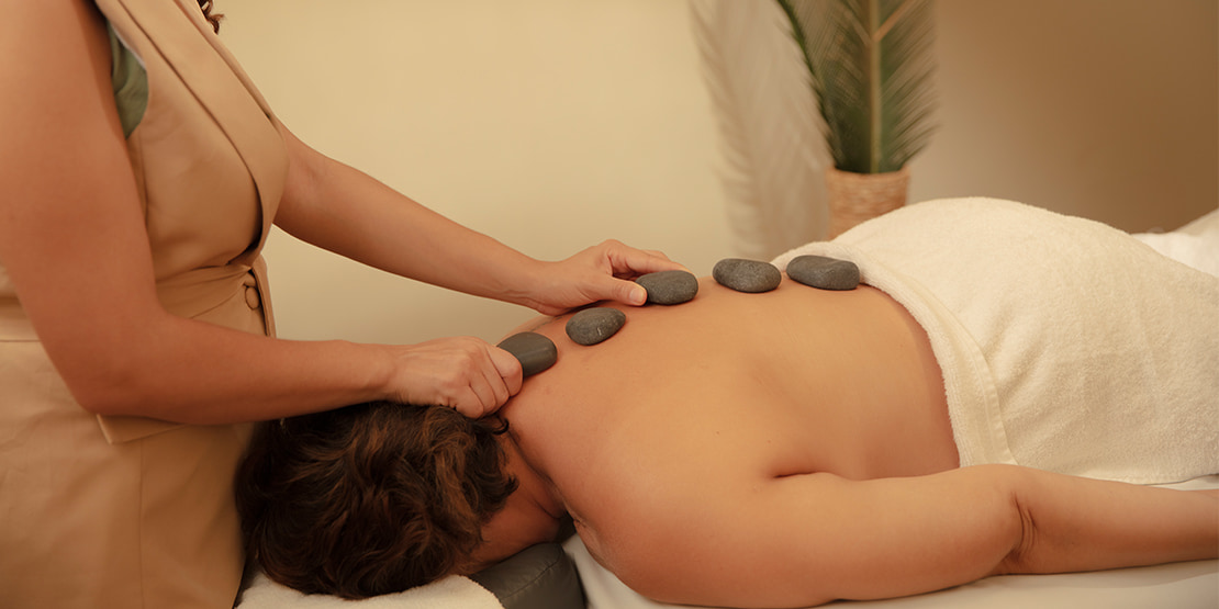 mulher deitada fazendo massagem com pedras quentes no spa